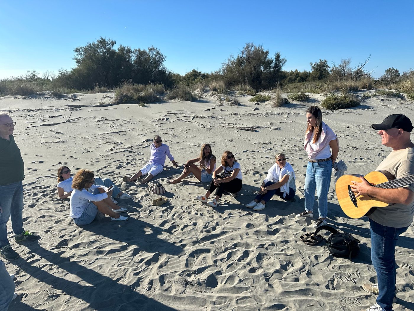 Gruppo di persone sedute in cerchio sulla spiaggia di Scano Boa mentre ascoltano una chitarra