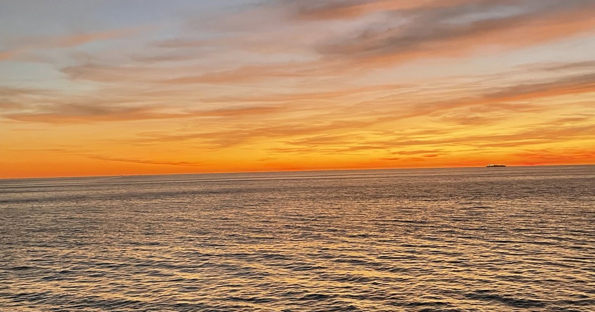 Sonnenaufgang über der Adria vom Boot aus, orangefarbener Himmel und ein Schiff am Horizont